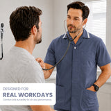 Uk Scrub Supply A man in a navy blue scrub top stands in a clinic setting with a stethoscope around his neck, speaking with another man. A white text box at the bottom left reads 'DESIGNED FOR REAL WORKDAYS Comfort and durability for all-day performance.